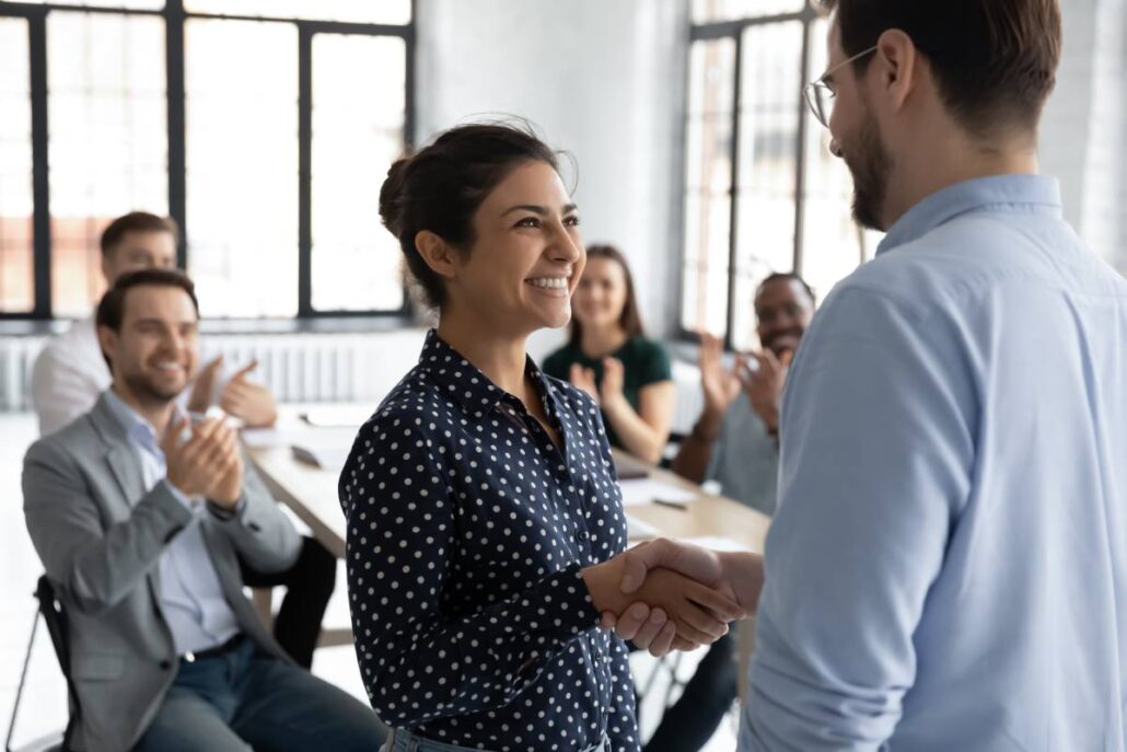 An employee receiving praise from their boss and cheers from fellow staff