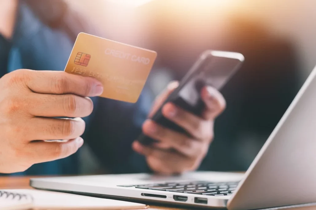 A person on their phone and laptop while holding a credit card