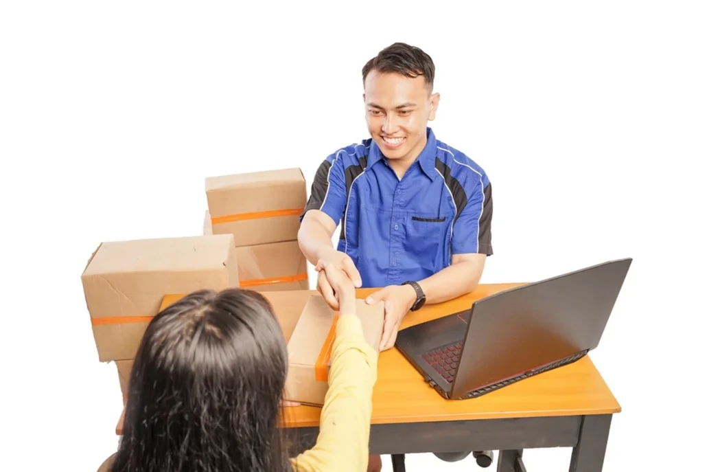 A man in a uniform behind a desk, shaking hands with a courier.